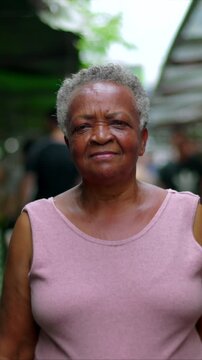Senior African American woman standing before open-air market stalls looking straight into the camera, carrying quiet dignity, resilience, and a grounded presence