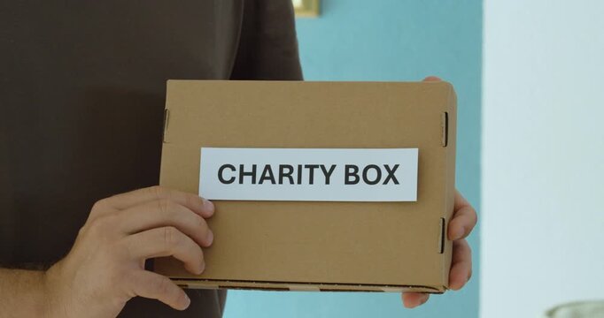 Close-up of a man holding and presenting a charity box, representing donations, fundraising, generosity and humanitarian support.