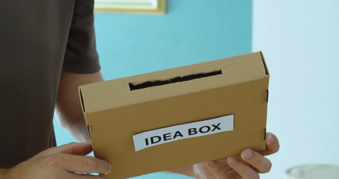 Close-up of a man holding and showing an idea box, demonstrating a simple system for collecting ideas, suggestions and employee feedback.