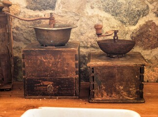 Two vintage manual wooden coffee grinders sitting on a rustic kitchen counter - Antique hand-crank coffee mills displayed as rustic farmhouse decor against a stone wall © light