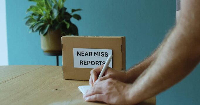 Man filling out a near miss report for a safety reporting box, representing workplace safety, accident prevention and hazard reporting.
