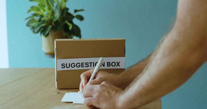 Person submitting a paper into a suggestion box, representing feedback, ideas, employee participation and workplace improvement.