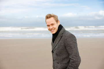 Smiling man in gray coat on beach © FOLIO
