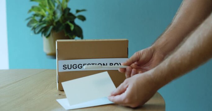 Man explaining how to write improvement ideas and submit them into a suggestion box, representing continuous improvement and employee feedback.