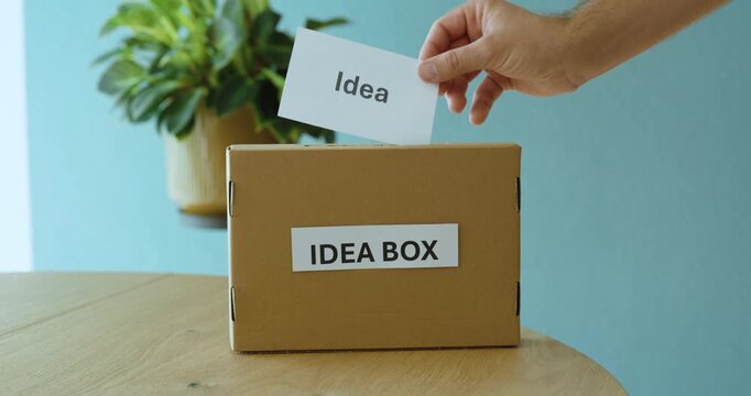 Person submitting an idea card into an idea box, representing innovation, suggestions, feedback and employee participation.
