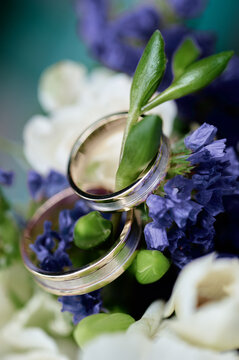 Close-up of wedding rings nestled in a bridal bouquet of purple statice and white blooms with fresh green leaves, conveying romance, commitment and elegant floral wedding detail.