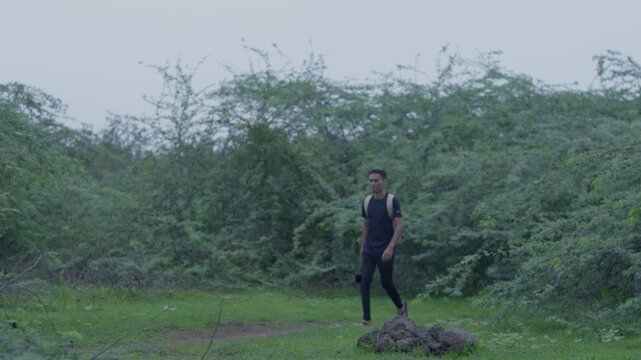 Wide shot of four young male friends with backpacks walking along a grassy path surrounded by lush green tropical bushes and trees.