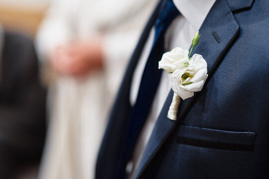 Close-up of a groom's navy suit adorned with a white boutonniere, highlighting delicate floral detail and the formal, elegant atmosphere of a wedding ceremony and celebration.
