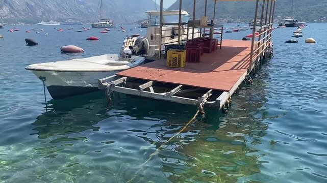 Small utility boat is moored alongside a floating wooden platform at an aquaculture farm in a scenic bay