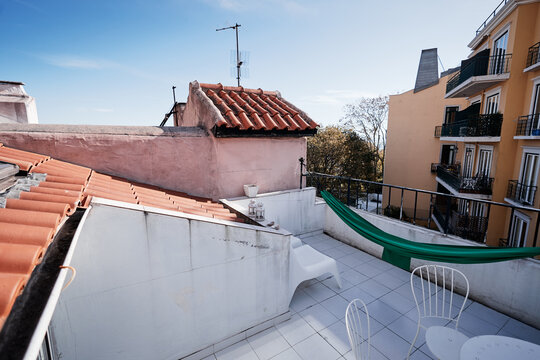 A rooftop terrace with a hammock, white chairs, and a view of neighboring buildings.