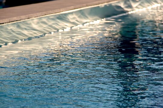 Low angle shot of rippling clear blue water along an infinity edge pool under bright sunlight reflections.