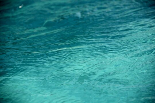 Abstract close-up of clear turquoise pool water with soft ripples and gentle sunlight reflections.