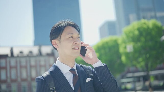 Japanese businessman smiling during a phone call under green trees