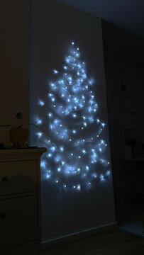 White string lights arranged in the shape of a Christmas tree glow on a wall in a dark room