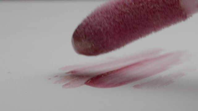 Makeup applicator coated with red cosmetic powder hovering above a white surface. Soft pigment marks and fine applicator texture create an abstract beauty closeup.