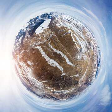 A tiny planet style panoramic view of snow-dusted mountain terrain under clear blue sky with sunlight.