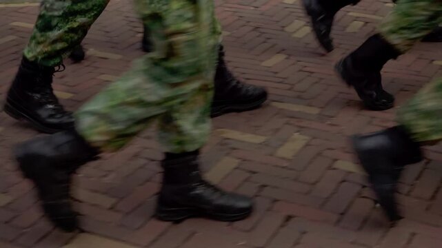Low angle closeup of military boots and camouflage trousers stepping over traditional brick pavement as armed forces march during Airborne commemorative event in Oosterbeek.