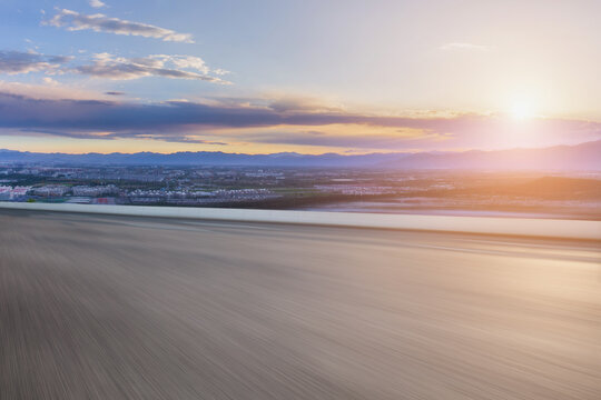 A wide flat open ground overlooks a distant city and mountain range under a colorful sunrise sky.