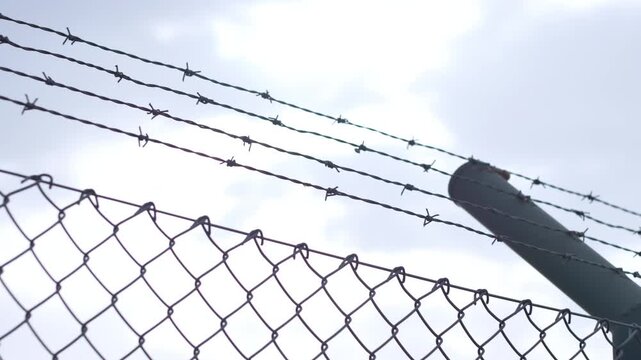 Horizontal pan showing razor barbed wire along the top of a security fence against a dramatic cloudy sky. Ideal for security, boundary, protection, and border concepts.