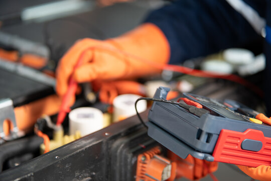 Testing an electric vehicle battery pack up close, a gloved hand touches a red probe to the fuses beside the tester.