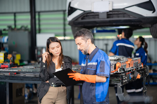 Thoughtful customer at the garage weighs the service report a technician explains beside the open electric car battery pack.