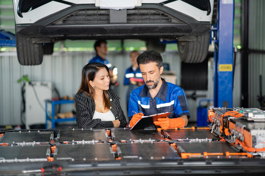 At the garage, a customer watches the service technician write on the battery inspection form clipped to his board.