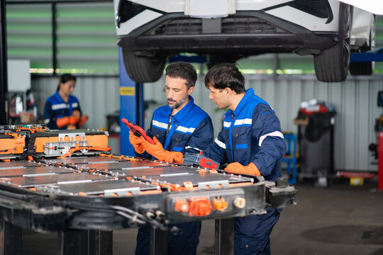Reading electric vehicle battery data on a tablet, a technician stands beside a colleague holding an insulation tester at the pack.