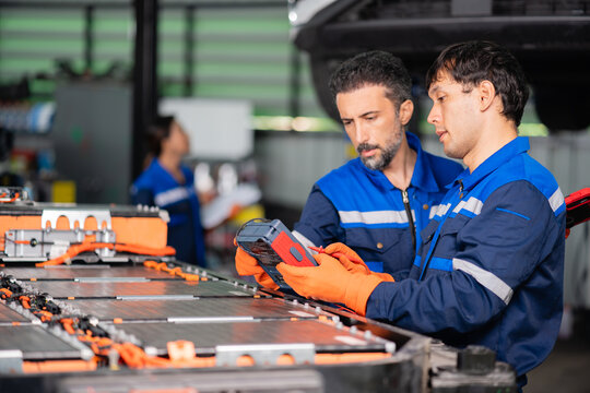 Checking electric vehicle battery readings on an insulation tester, a technician works while a colleague looks on closely.