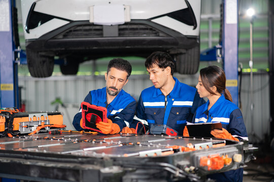 Electric vehicle battery results on a tablet draw three technicians together over the open pack at an EV service bay.