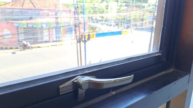 Closed black window latch with view of street and traffic outside. Window, home, building, urban view, looking out, sunlight, city, residential, architecture.