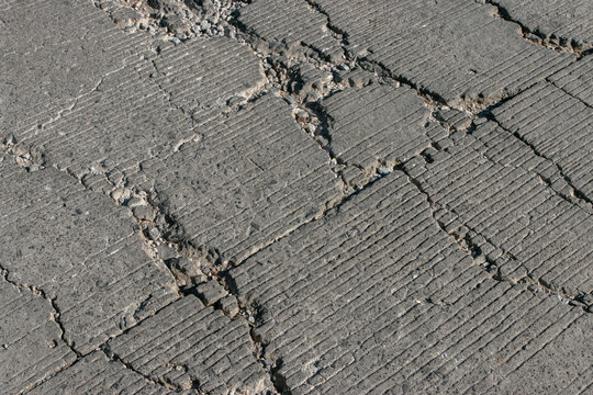 A close-up of cracks on a concrete road surface, revealing damage, potholes, and signs of wear; ideal for illustrating concepts such as infrastructure damage, maintenance, transport safety, and urban 
