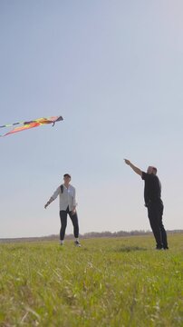 Young caucasian couple unsuccessfully attempting to launch a colorful kite on a windy day, laughing together in a vast green meadow under a clear blue sky during their fun outdoor activity