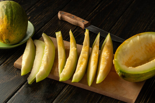 Bright green melon slices rest on a wooden board, showcasing their fresh, juicy interior. A knife and whole melon sit nearby, suggesting preparation for sharing or enjoying