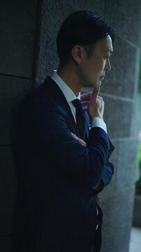 Businessman with a hand on his chin thinking beside a stone wall