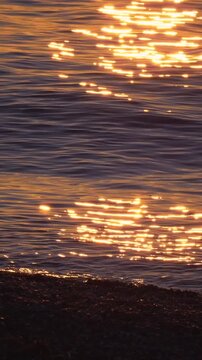 Pebble beach beside calm sea at sunset, with sunlight on gentle waves. Peaceful shoreline for slow travel, mindfulness and digital detox. Vertical video.