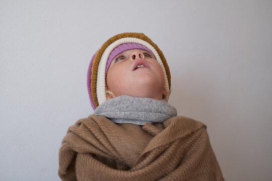 Little girl wrapped in warm brown scarf looking up wearing layered winter hats