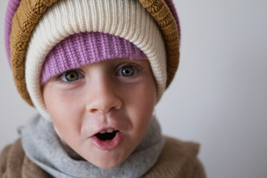  surprised little girl wearing multiple warm winter knitted beanies