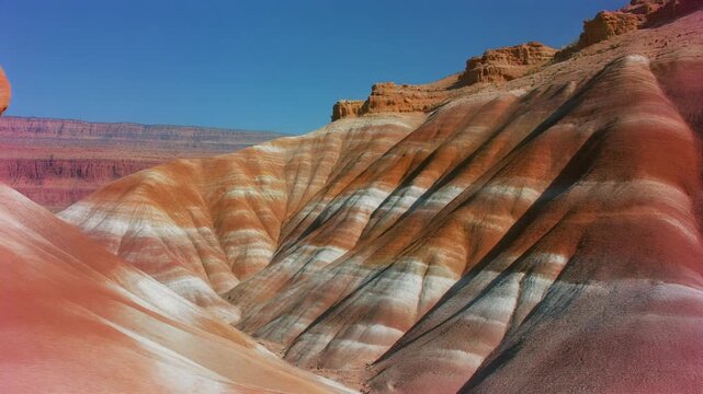 Striped desert mountains landscape video. High angle view of red and white sediment layers in badlands canyon under clear blue sky. Cinematic geological footage for nature and travel content.