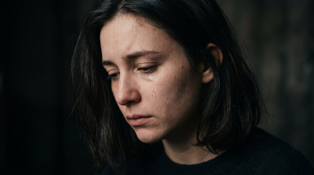 Sad young woman crying with a tear on her cheek in dark moody lighting