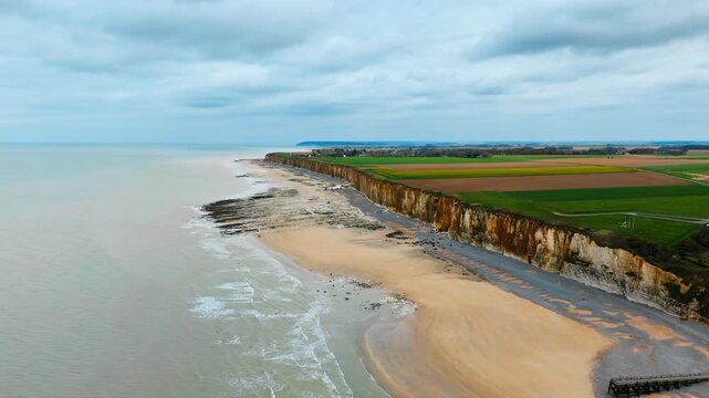 High chalk cliffs run along Normandy coast above beach and calm sea. Coastal erosion, marine geology and changing shoreline