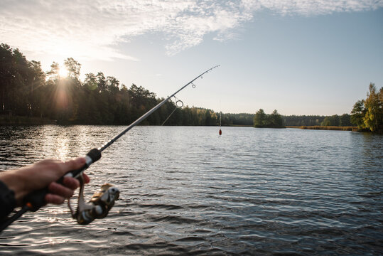 Fisherman holding a spinning rod with lure over a scenic lake, enjoying quiet angling on Fisherman's Day from a pier, boat, or shore during golden hour.