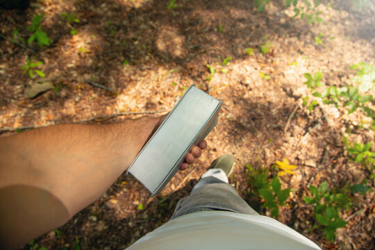 Male hand showing book in the forest.