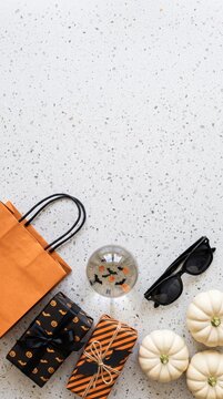 halloween gift boxes with orange shopping bag white pumpkins and sunglasses on white terrazzo surface