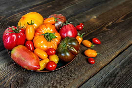 Assorted fresh heirloom tomatoes in a bowl on a rustic wooden background.