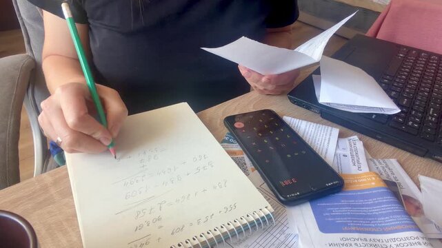 Woman calculating expenses and writing notes at desk