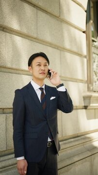 Japanese businessman on a serious phone call beside a stone office building
