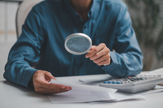 Auditor holding magnifying glass to inspect financial document beside calculator for corporate fraud investigation and compliance audit