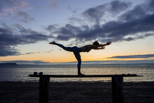 White person balancing in warrior iii yoga pose on beach bench