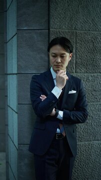 Thoughtful businessman looking down while leaning against a stone wall