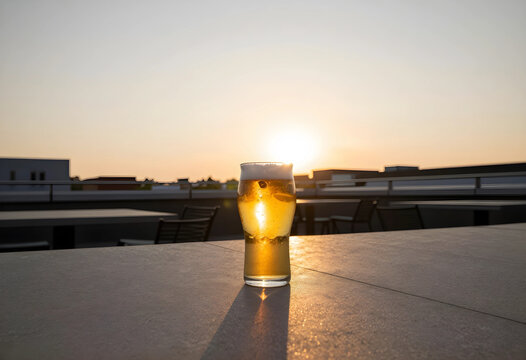 Relaxation and leisure lifestyle, glass of cold beer on a rooftop terrace during golden hour sunset with urban city skyline background and warm light